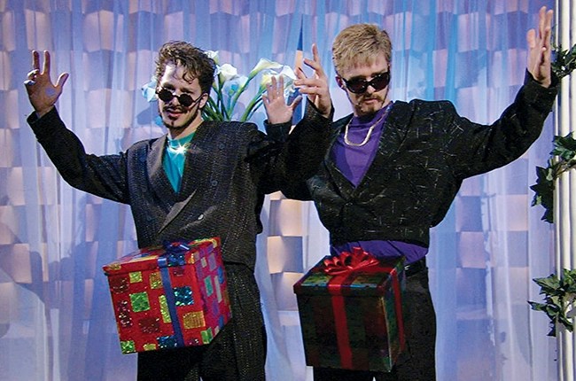 Andy Samberg and Justin Timberlake wearing sunglasses, gold chains, and presents on their crotches.