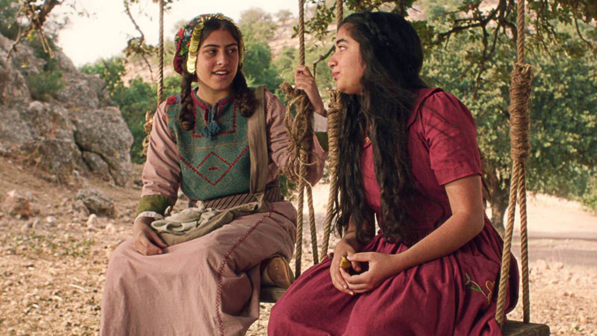 Two Palestinian girls sit in swings with trees behind them in Farha.