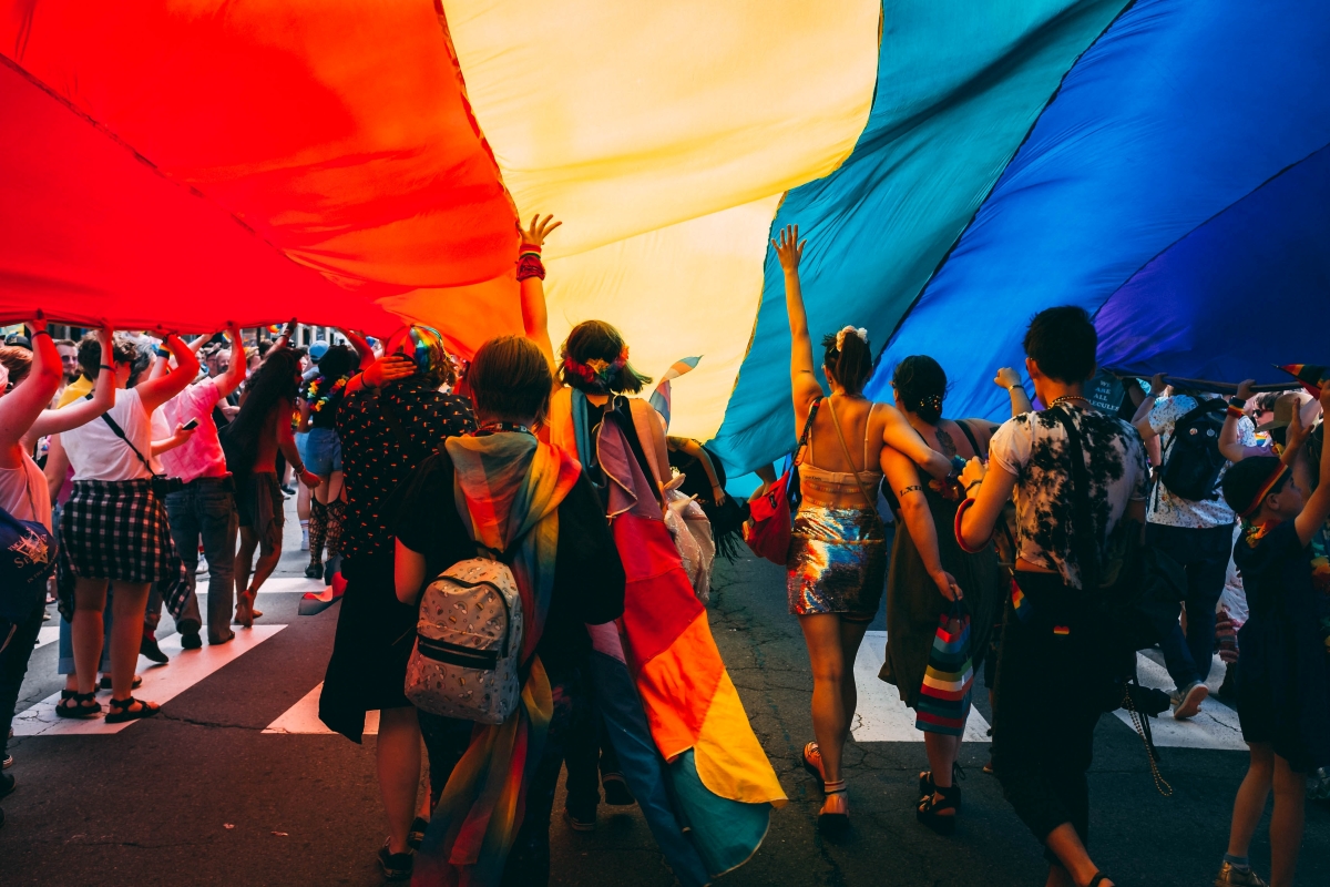 People walk under a LGBTQ+ Pride flag