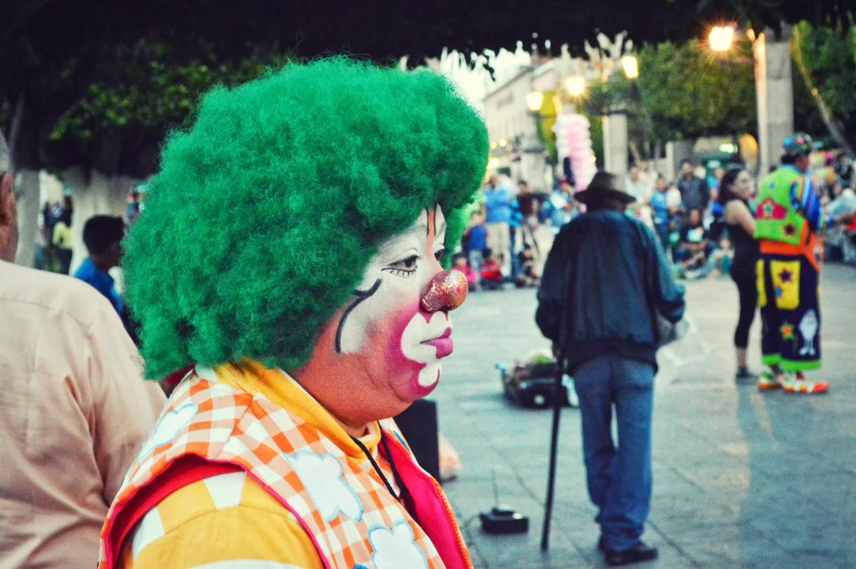 A clown in a green wig, standing on a street corner.