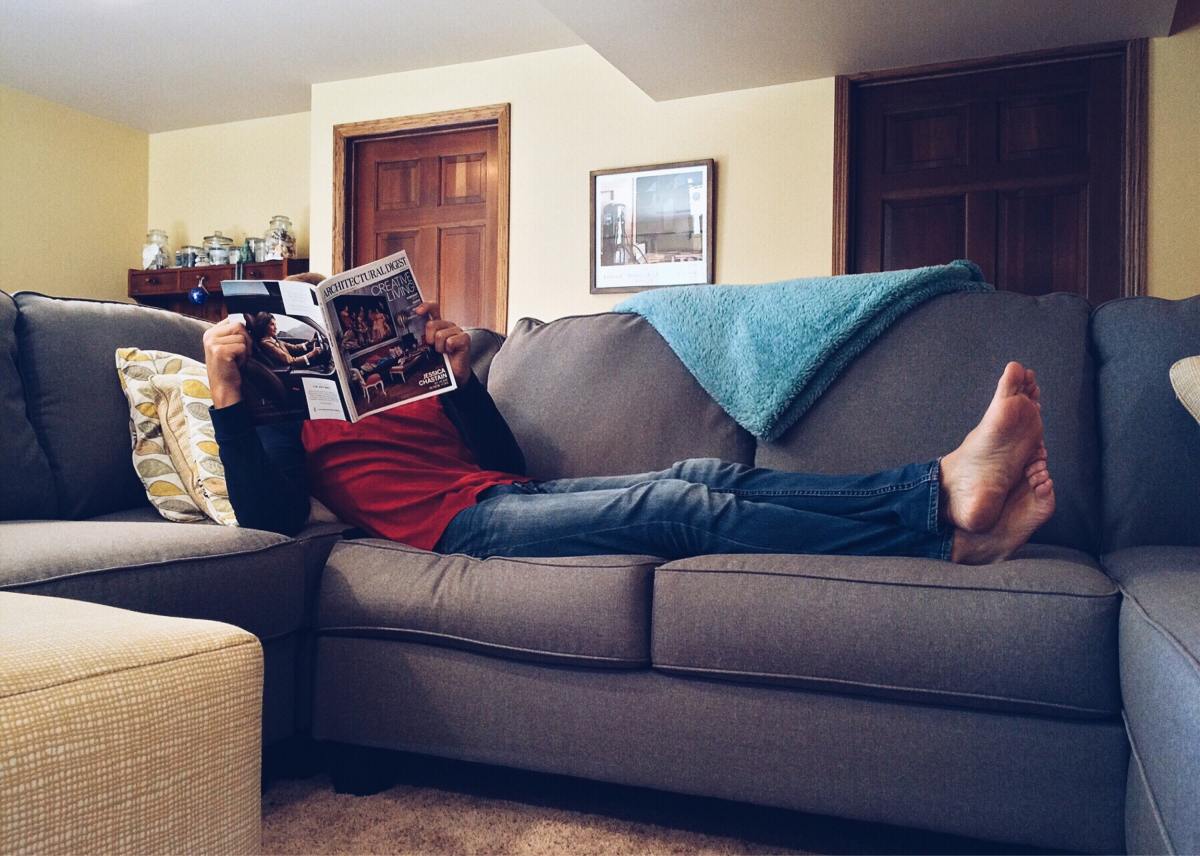 Someone lying on a couch, their face obscured by a newspaper.