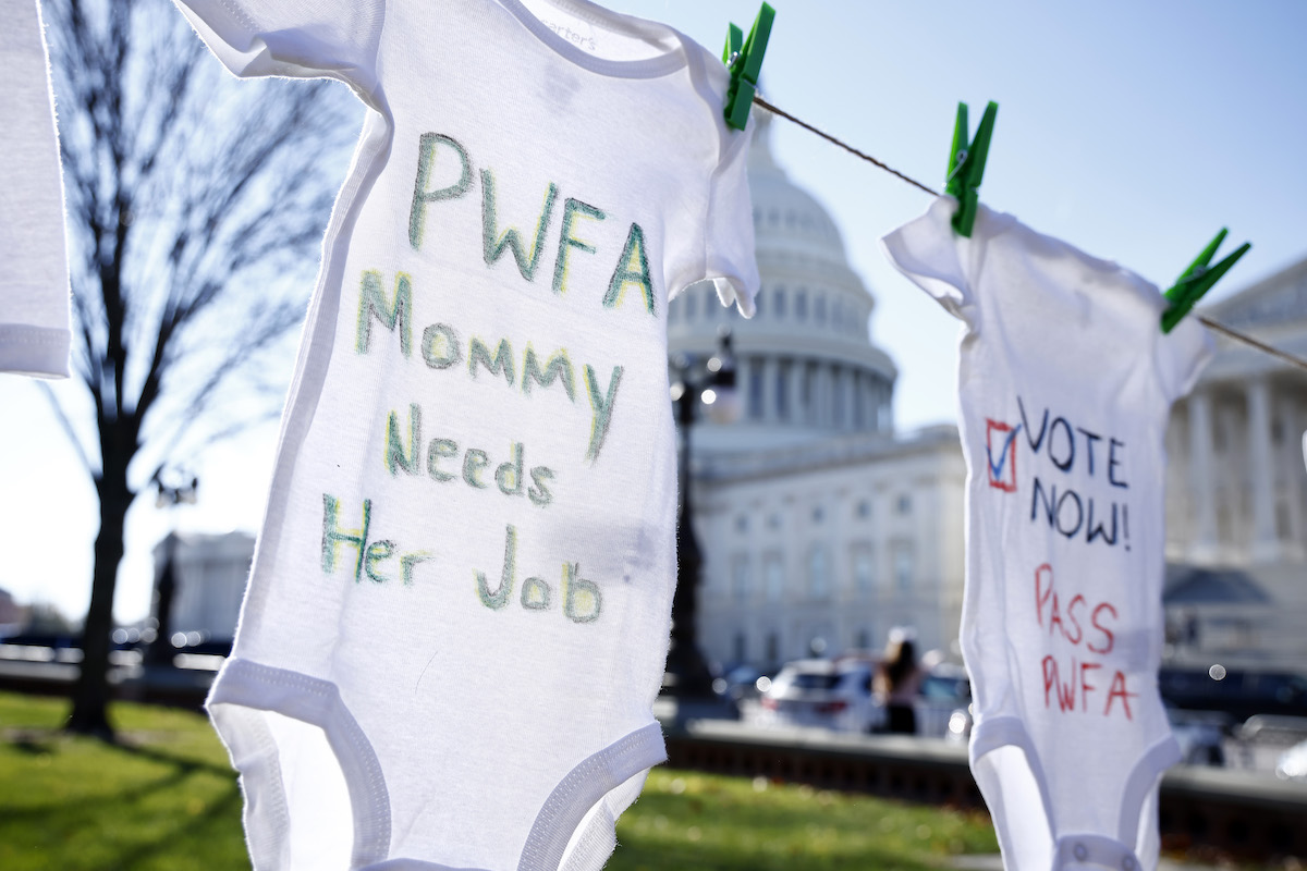 Babies onesies with messages written on them like 'PWFA Mommy needs her job' hang on a clothesline in front of the Capitol building