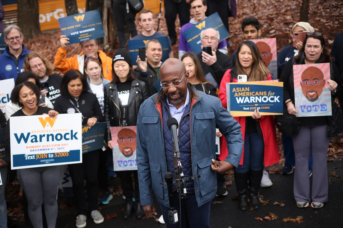 Raphael Warnock stands in front of a group of supporters holding campaign signs.
