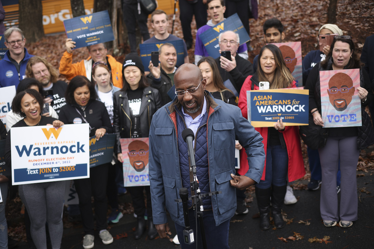 Raphael Warnock stands in front of a group of supporters holding campaign signs.