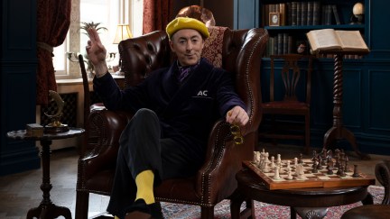 Actor Alan Cumming wears a fashionable ensemble topped with a yellow beret as he sits in a study in an image promoting his new reality competition series 'The Traitors'