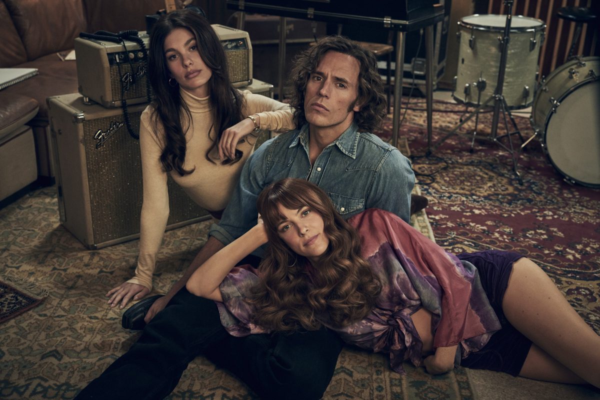 Two women and a man sit on the floor of a music studio, dressed in 1970s styled clothes.