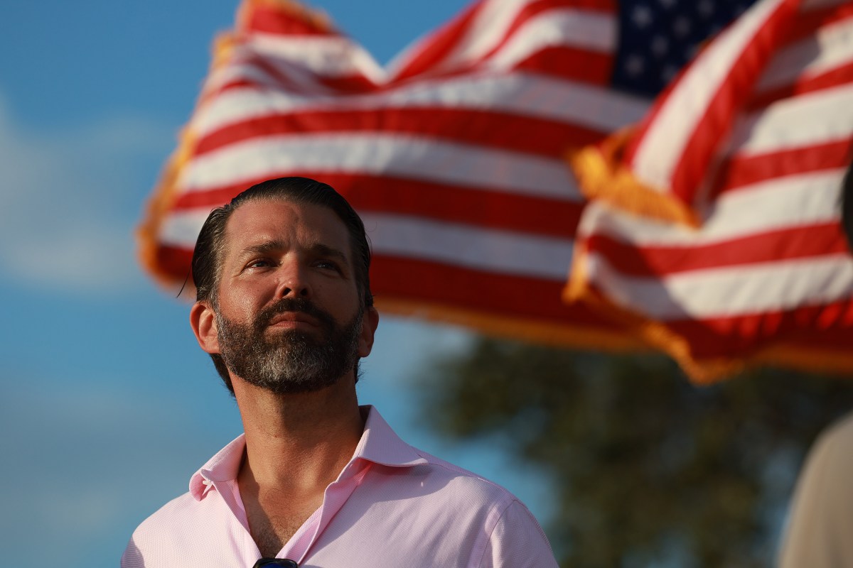 Donald Trump Jr. stares into the distance in front of an American flag.