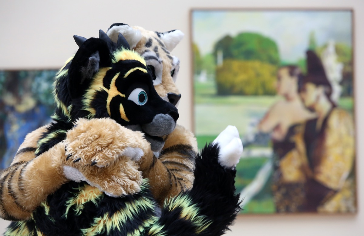 Two people in fur suits hug each other in front of a piece of artwork at the Eurofurence conference in 2015