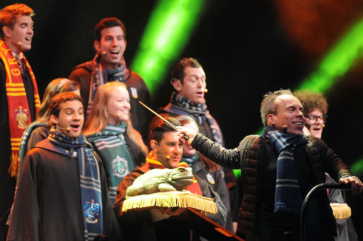 Actor Warwick Davis conducts a group of singers dressed in Harry Potter robes and scarves.