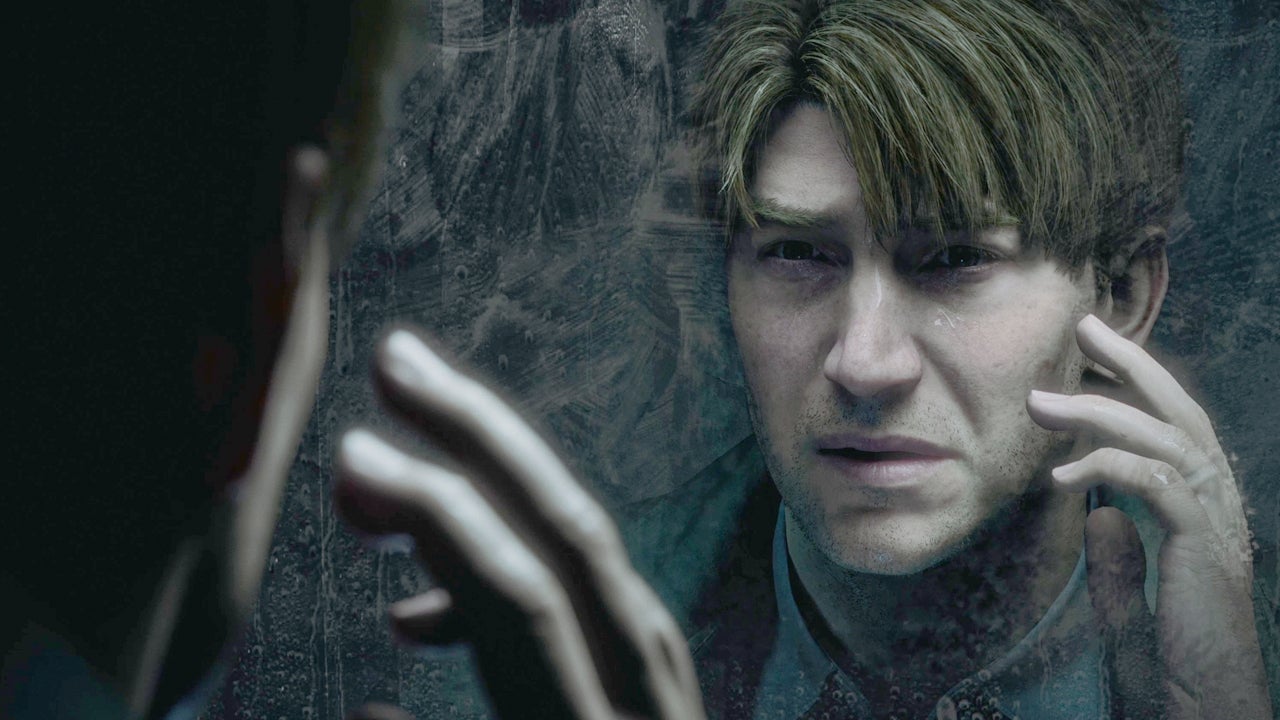 In an image from 'Silent Hill 2,' a disoriented James touches his face with his hand while looking into a mirror.