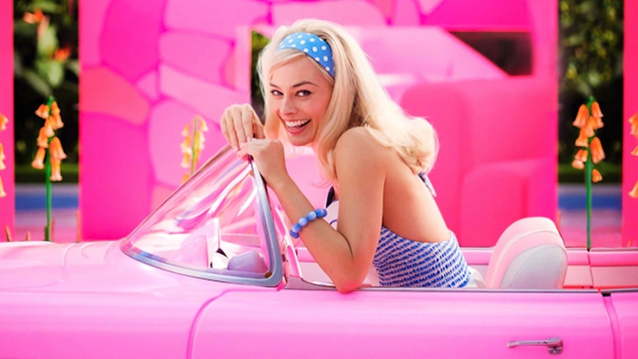 Margot Robbie's Barbie gives a big smile while sitting in a pink Corvette 