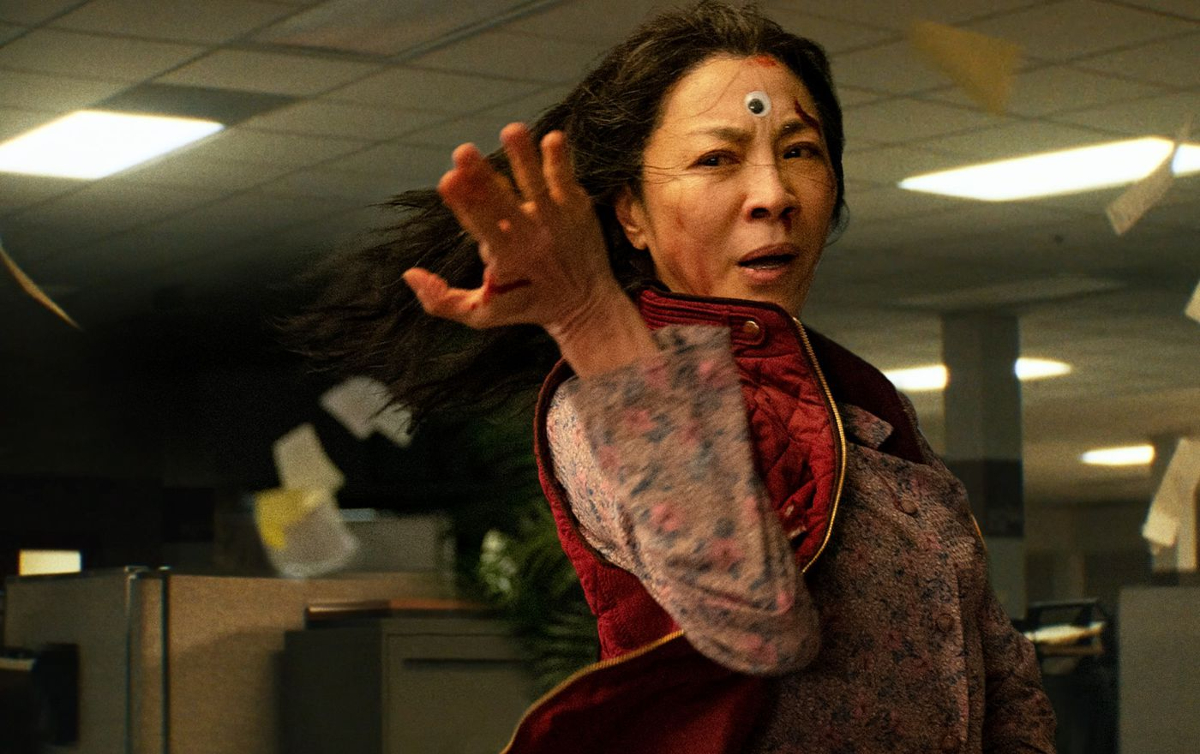 Evelyn (Michelle Yeoh) takes a fighting stance in a scene from 'Everything Everywhere All at Once.' She's standing in an office filled with cubicles and one of those googly eyes is attached to the center of her forehead.