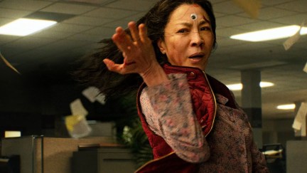 Evelyn (Michelle Yeoh) takes a fighting stance in a scene from 'Everything Everywhere All at Once.' She's standing in an office filled with cubicles and one of those googly eyes is attached to the center of her forehead.