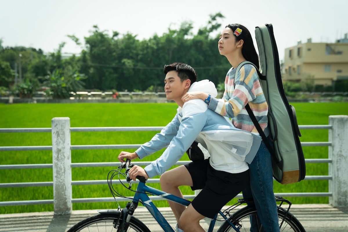 A teen boy riding a bicylcle on a country road and a teen girl wearing a guitar case riding with him in a scene from 'My Best Friend's Breakfast'