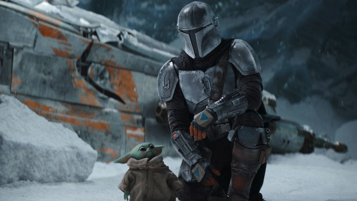 Din Djarin (Pedro Pascal) kneels in the snow alongside Grogu in an image from 'The Mandalorian.'