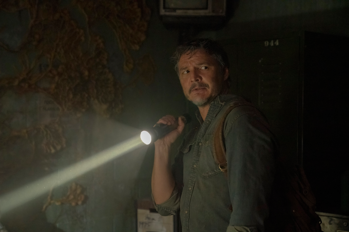 Joel Miller (Pedro Pascal) stands in a dark room, holding a flashlight in a still from 'The Last of Us'