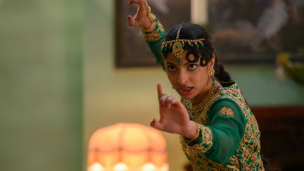 Ria Khan (Priya Kansara) prepares for battle in a still from 'Polite Society.' Ria wears a green dress with gold embellishments and a gold headdress.