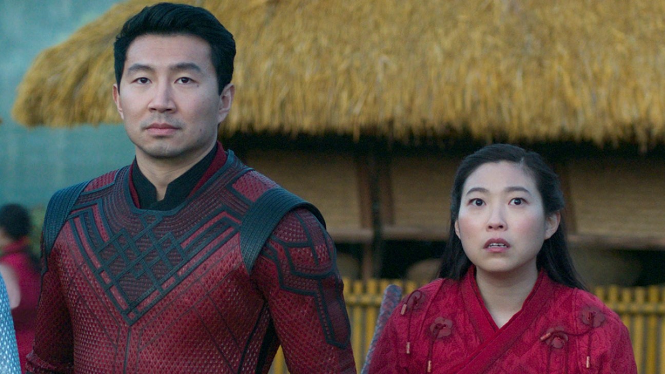 Shaun/Shang-Chi (Simu Liu) stands next to his friend, Katy (Awkwafina) in a scene from 'Shang-Chi and the Legend of the Ten Rings.' They have  concerned looks on their faces in response to something we cannot see.