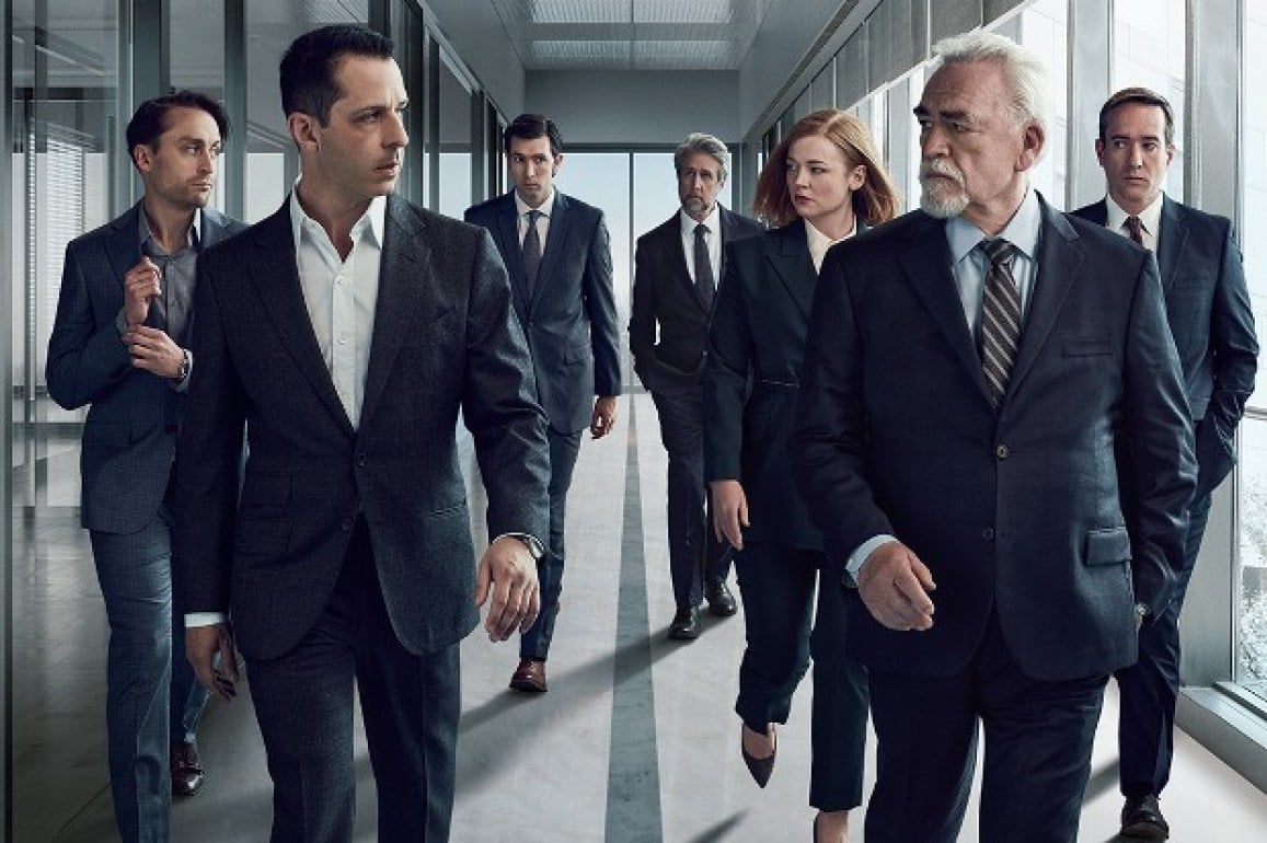 Members of the Roy family from the series, Succession, walk through a halfway of an office looking intently at one another.