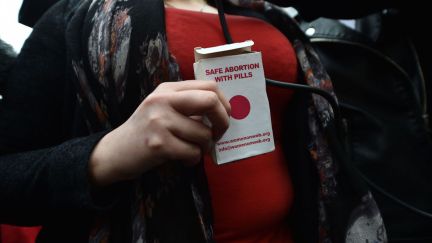 A woman holds an abortion pill packet in front of her