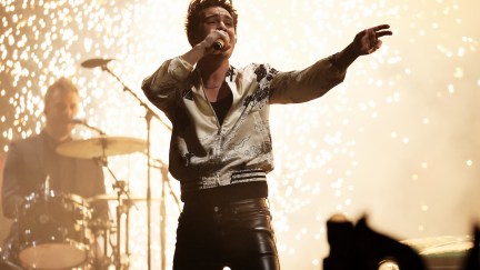 Brendon Urie sings into a microphone with sparks behind him.