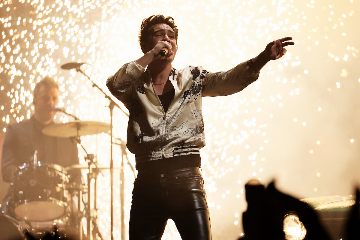 Brendon Urie sings into a microphone with sparks behind him.