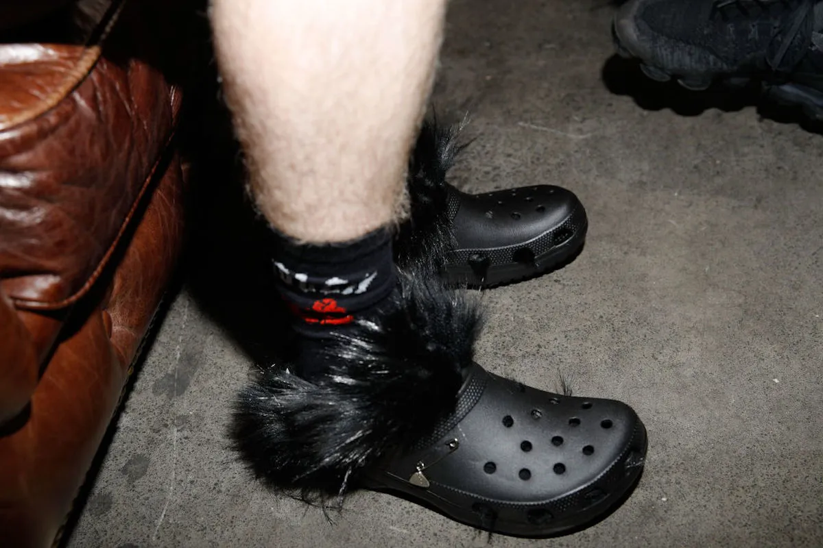 A pair of black Crocs wish black feathers on a white man's legs