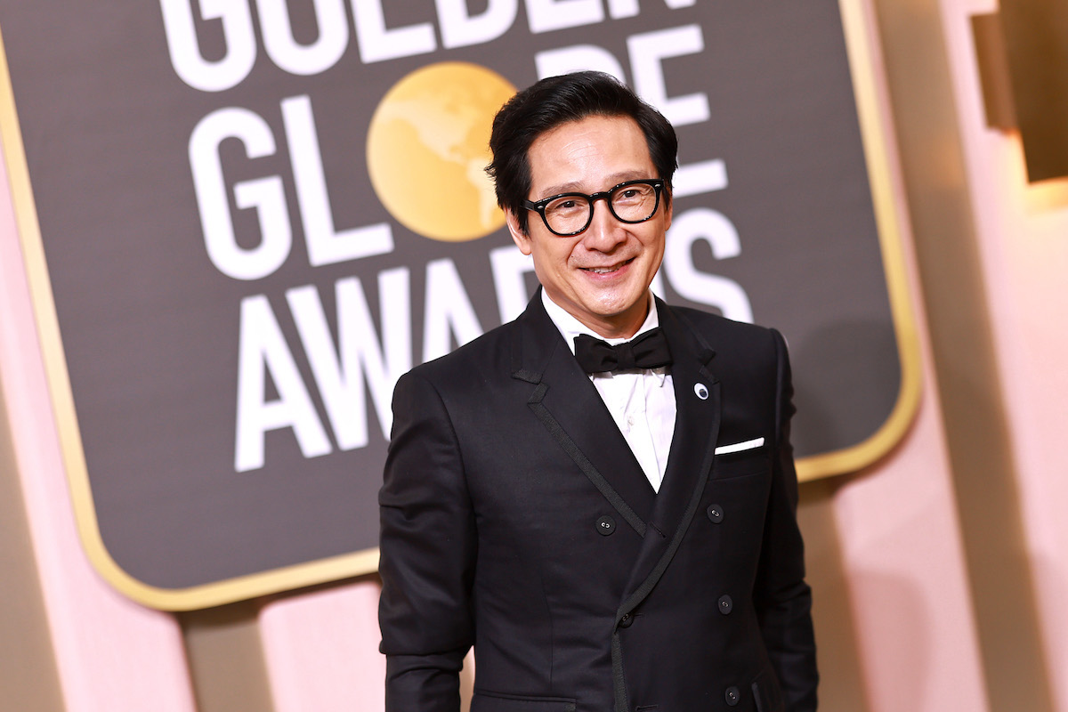 Ke Huy Quan smiles in a tuxedo with a Golden Globe Awards sign behind him.