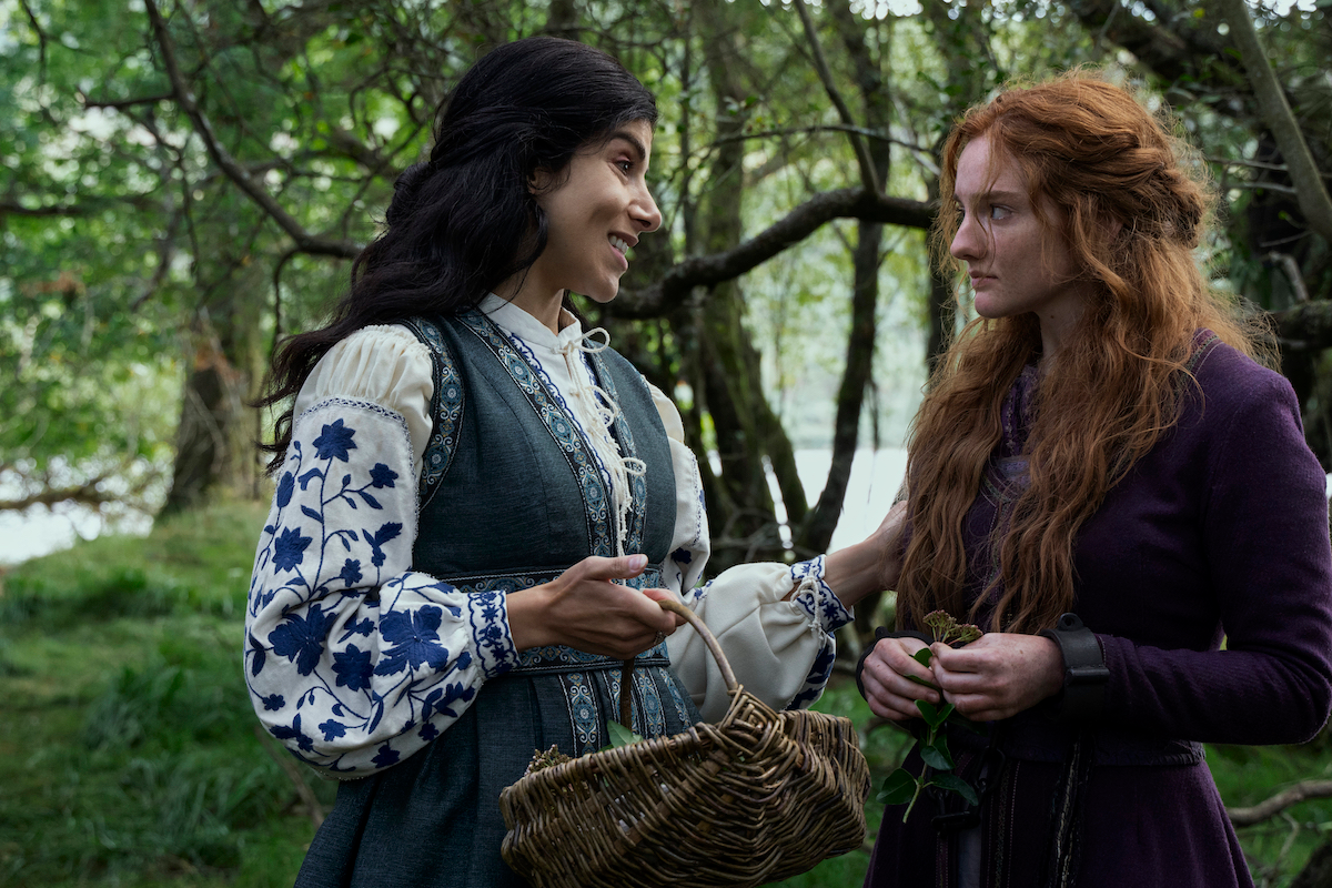 Mariam smiles at Dorn in Vikings: Valhalla season 2. Mariam wears a blue and white dress with embroidered flowers on the sleeves. Dorn has red hair.