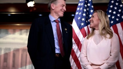 Marjorie Taylor Greene and Paul Gosar grin at each other while standing in front of an American flag.