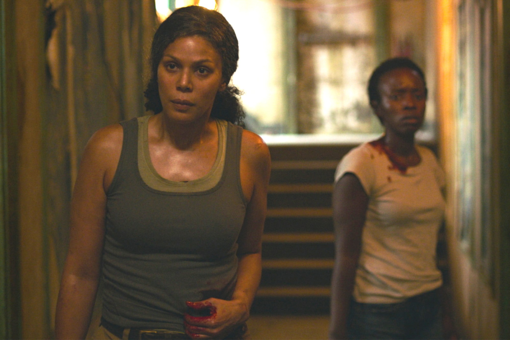 Marlene (Merle Dandridge) and Kim (Natasha Mumba) are standing in a hallway, bleeding from gunshot wounds in a scene from 'The Last of Us.'