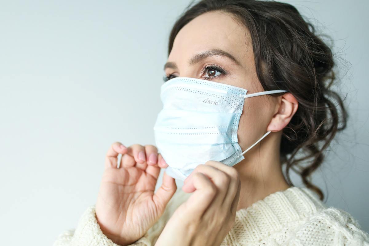 A brown-haired woman adjusts a surgical mask.