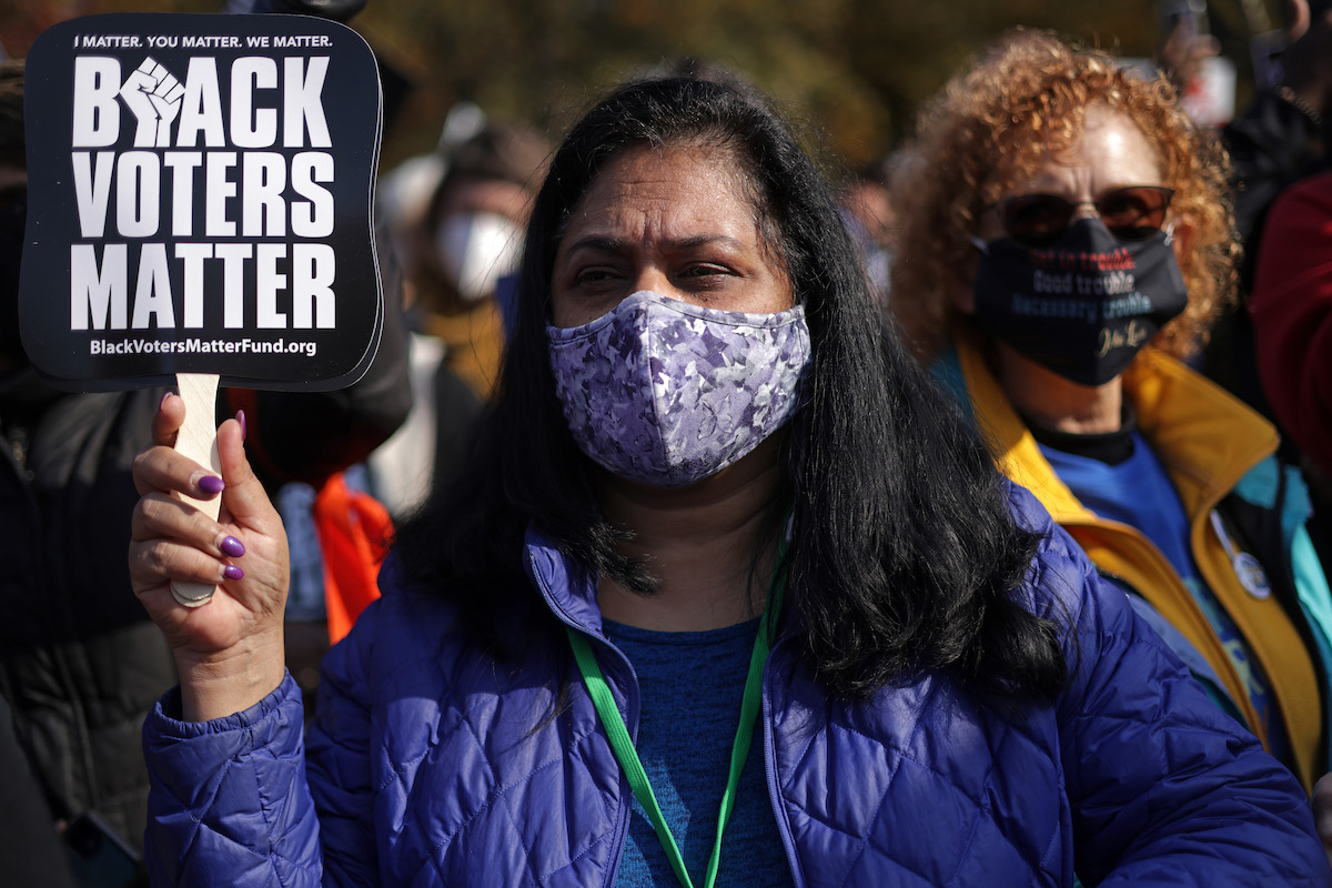 A protester wearing a face mask holds a small sign reading "black voters matter"