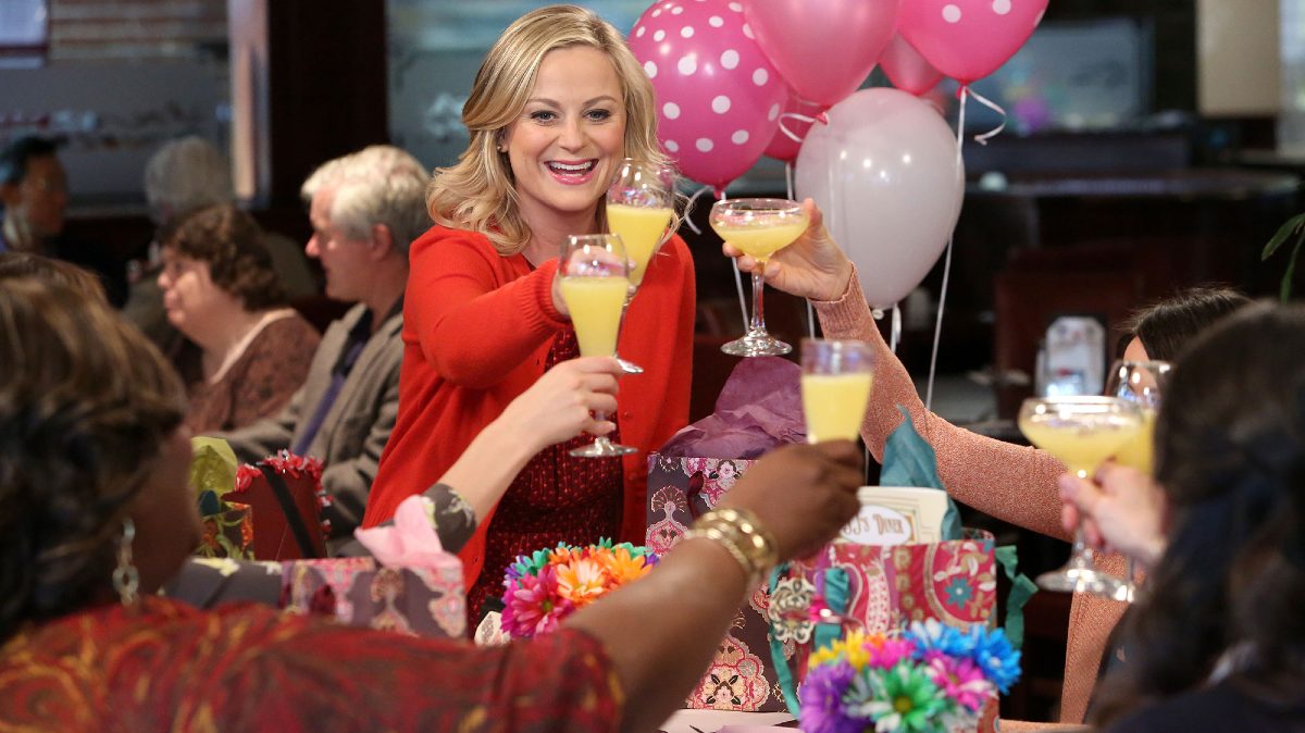 Leslie Knope (Amy Poehler) holds up a mimosa to cheers her friends at brunch on Galentine's Day