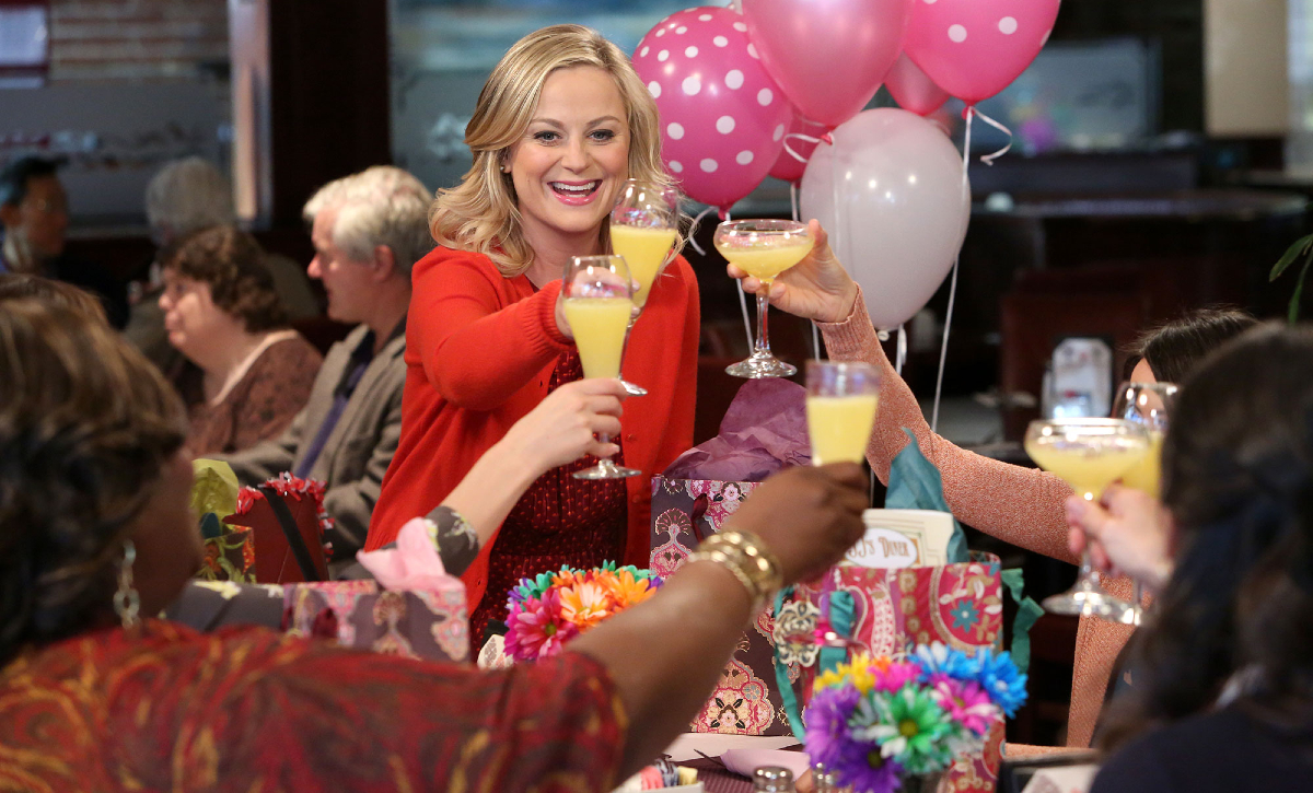 Leslie Knope (Amy Poehler) holds up a mimosa to cheers her friends at brunch on Galentine's Day