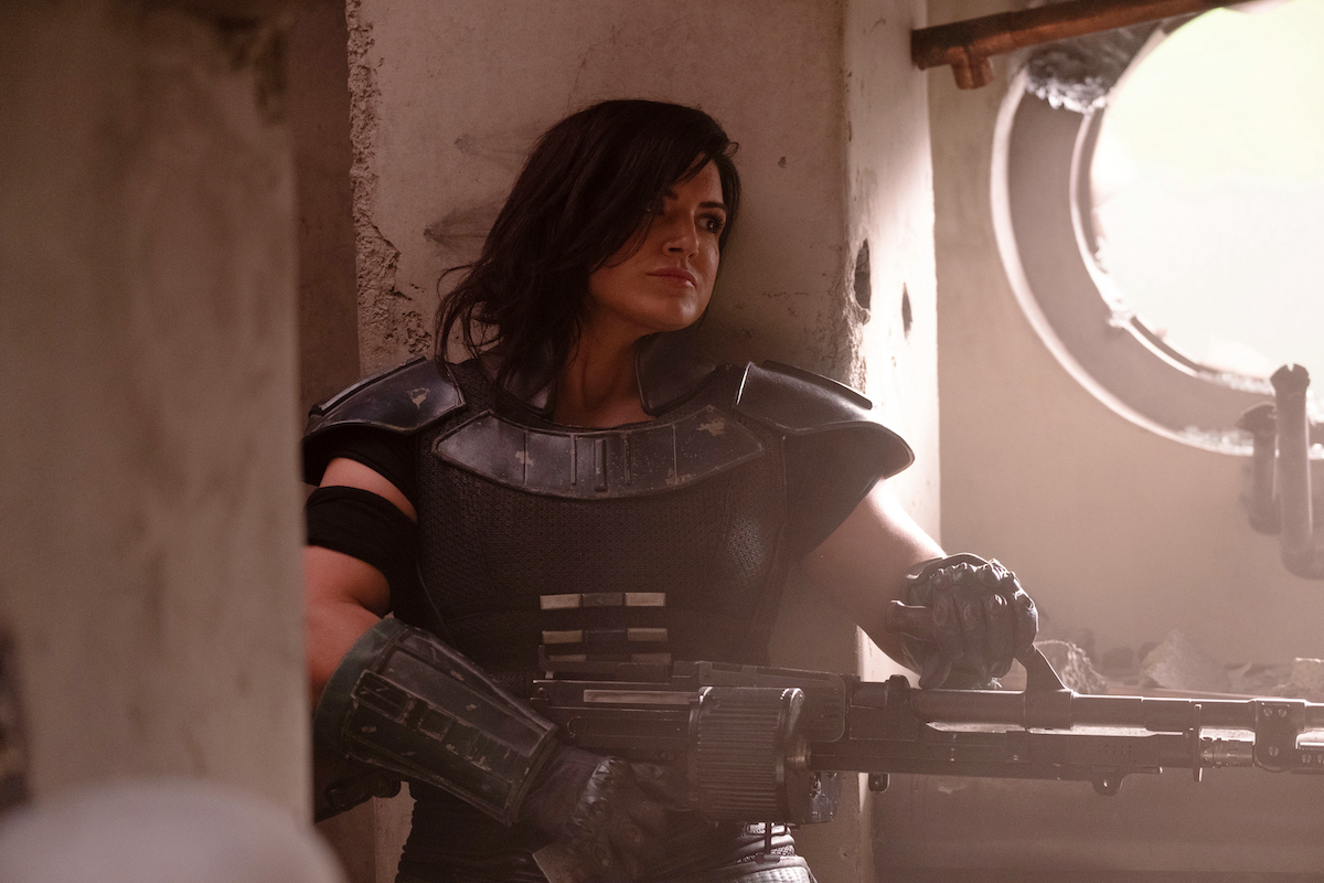 Gina Carano as Cara Dune in a battle scene in The Mandalorian, walking through a building, armed with a rifle