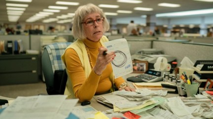 Jamie Lee Curtis as the character Deirdre Beaubeirdre in the film Everything Everywhere All at Once, sitting at her desk, which is covered in financial paperwork