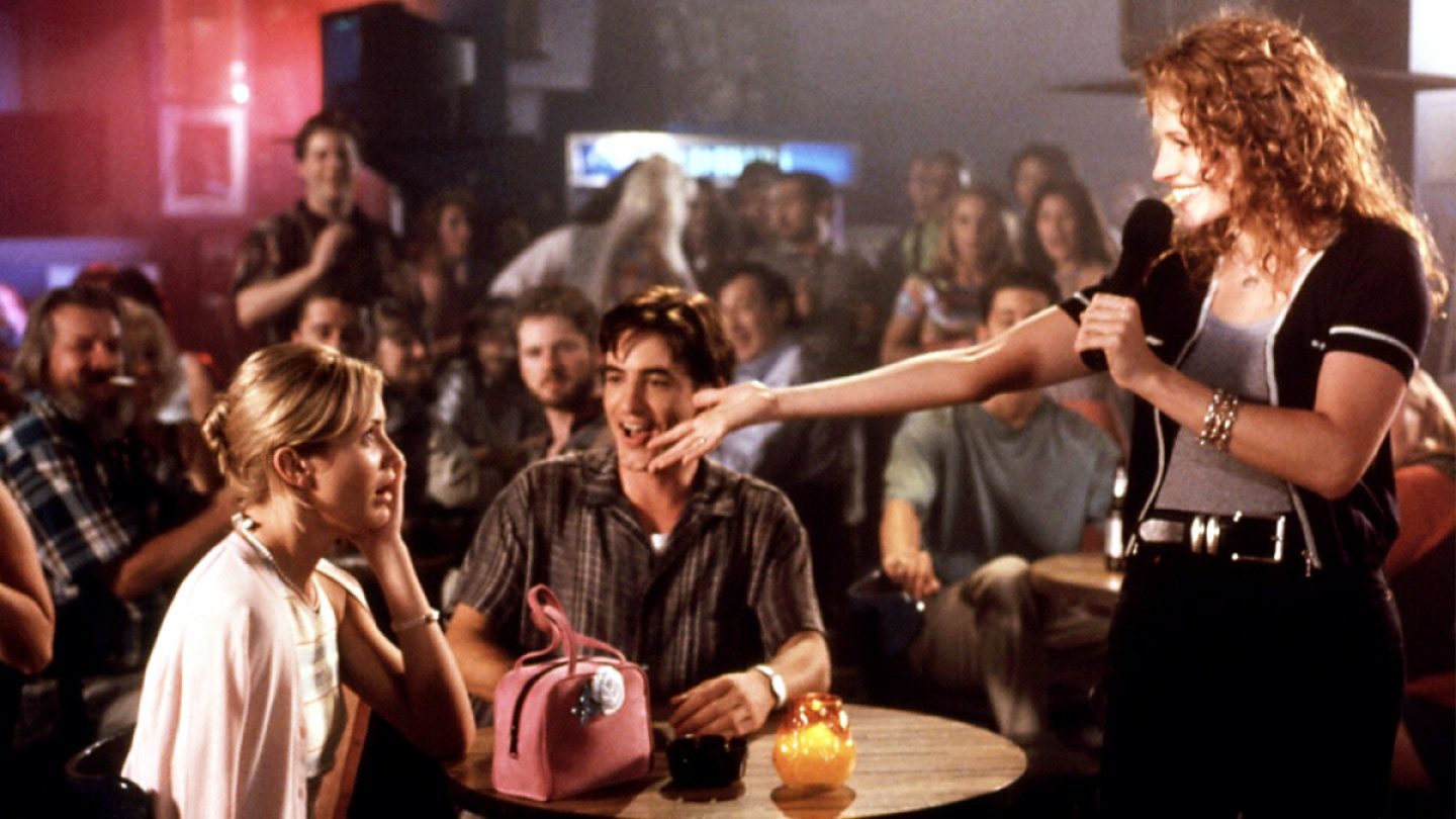 Julia Roberts serenades Cameron Diaz at a packed karaoke bar, as Dermot Mulroney watches.