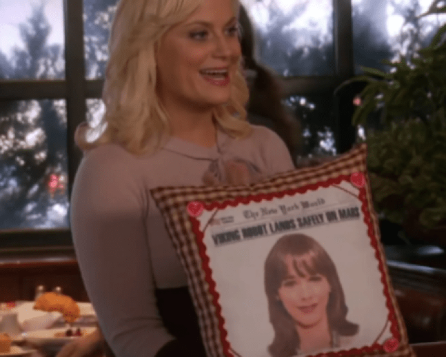 Leslie Knope stands with  a pillow of Anne Perkins' face on it