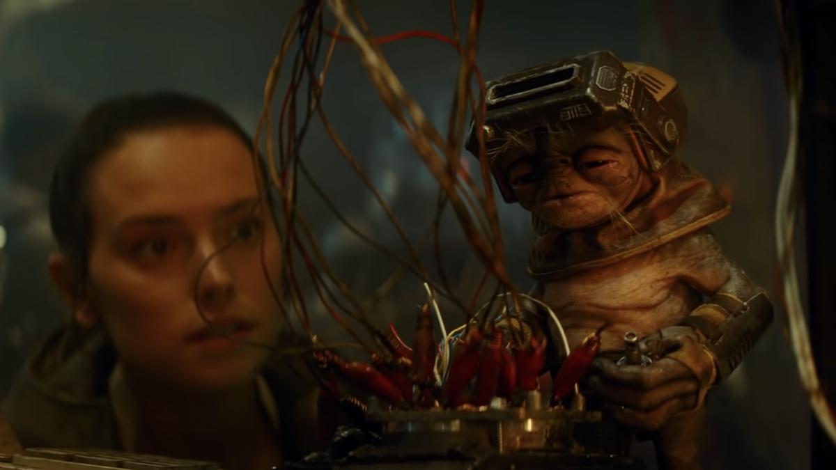 Daisy Ridley as Rey squatting behind the alien character Babu Frik, who is much smaller than her