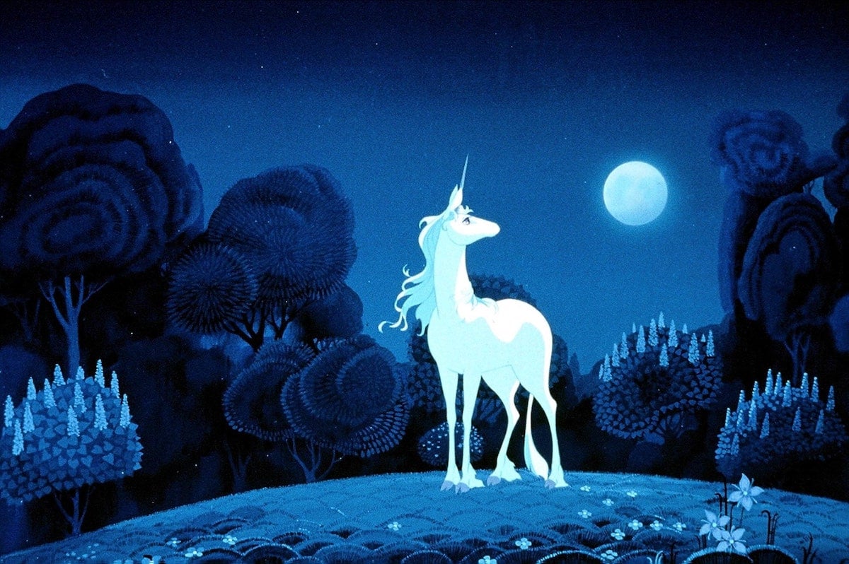 A still from the animated film The Last Unicorn that shows a white unicorn standing in a meadow under bright moonlight