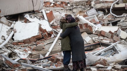 Two people embrace each other while standing near a collapsed building in Turkey following a 7.8-magnitude earthquake that devastated the region.