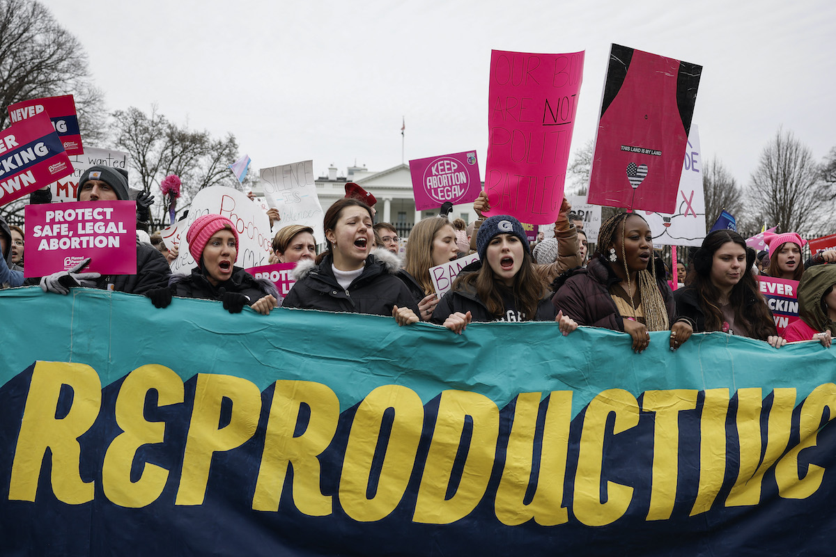 A group of abortion rights protesters carry a banner reading "reproductive" in large letters.