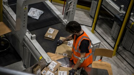 An Amazon employee collects packages from a conveyor belt.