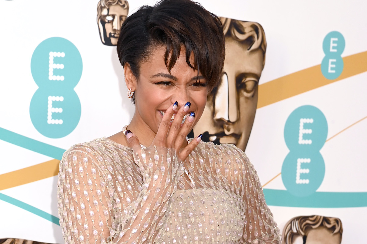 Ariana DeBose holds her hand over her mouth and laughs on the BAFTAs red carpet.