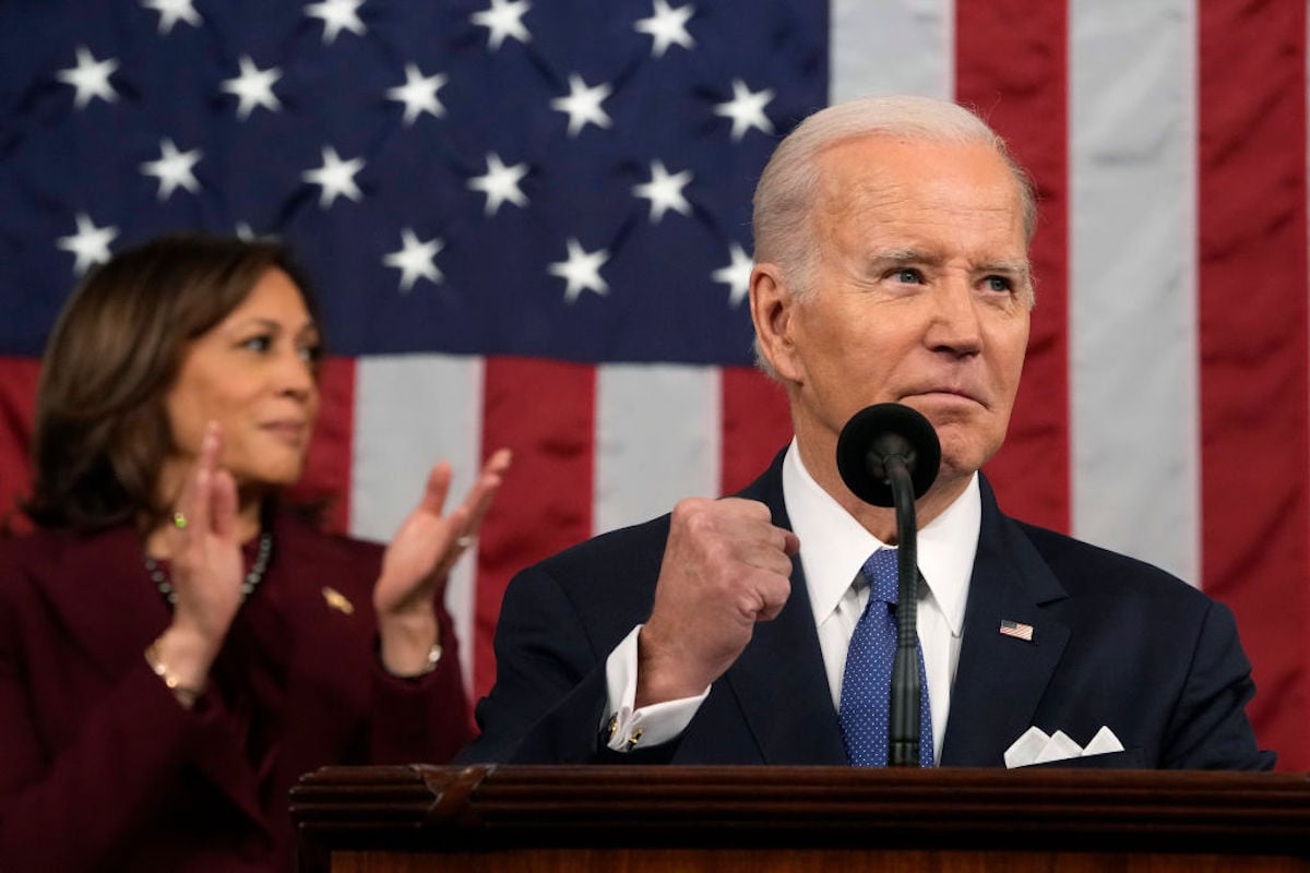 Joe Biden raises a fist while standing at a podium. Kamala Harrise claps behind him, standing in front of an American flag.