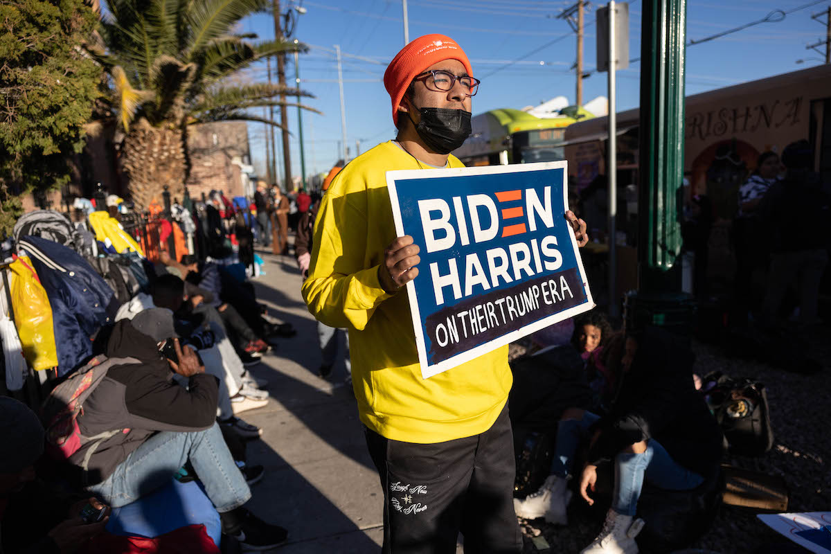 An immigration rights protester holds a Biden/Harris campaign sign with a handwritten tag reading "on their Trump era"