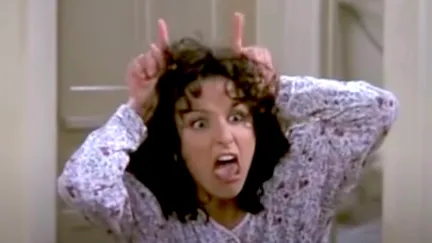 Elaine mimes devil horns on her head in Seinfeld.