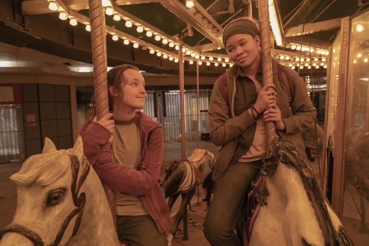 Ellie and Riley sit on merry go round horses, smiling at each other.
