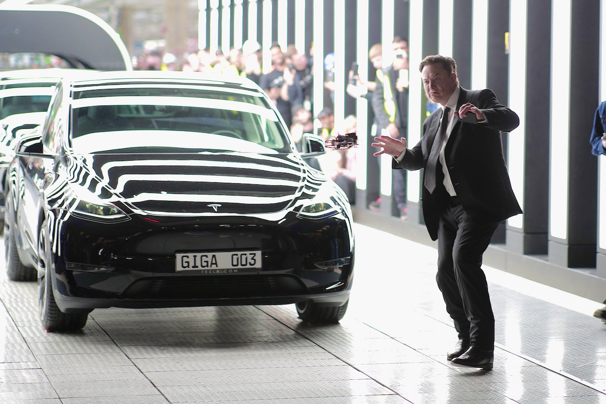 Elon Musk strikes a strange pose in front of a Tesla car.